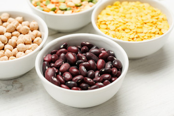 Different beans in bowls on a white wooden table