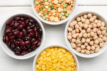 Different beans in bowls on a white wooden table, top view
