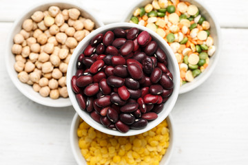 Different beans in bowls on a white wooden table, top view