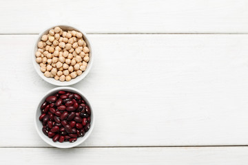 Different beans in bowls on a white wooden table, top view
