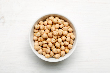 Chickpea in a white ceramic bowl on a wooden table, top view