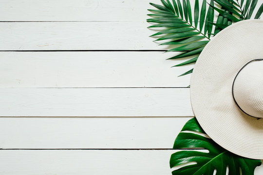 White straw hat, green plam leaves on wooden baclground. Summer holidays vacation concept. Poster banner, postcard template.
