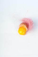 Yolk of broken egg in eggshell decorated with pink sisal nest on the minimalist white background