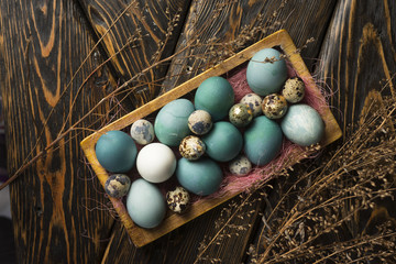 Blue, and white and chicken eggs and quail eggs in wooden retro style box decorated with a pink sisal and dried branches on vintage style wooden table covered with sackcloth.