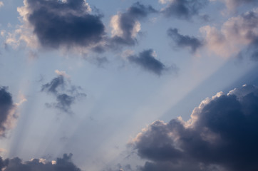 Wonderful sun rays penetrating through fluffy clouds on the blue sky in a hot summer day. Beautiful cloudscape background great for your graphic design project