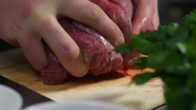 Tracking shot of hands of male cook cutting raw meat on wooden cutting board and taking it away when cooking pilaf, tracking right