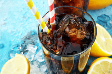 Softdrink with ice cubes, lemon and straw in glass.