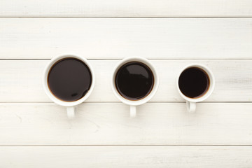 Various cups with black coffee on white wooden table