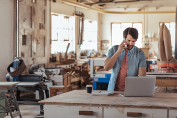 Woodworker using a phone and laptop in his large workshop