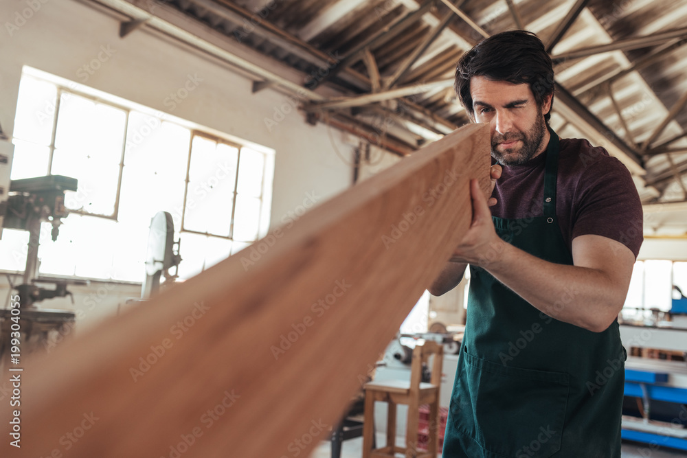 Wall mural Skilled craftsman examining a plank of wood in his workshop