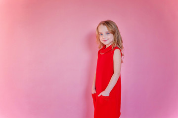 Little cute sweet smiling girl in red dress standing on pink colourful pastel trendy modern fashion pin-up background