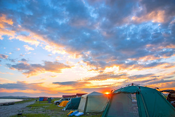bright red sunset over the beach, there are a number of tents. tourist camp