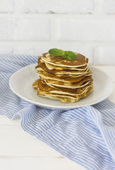 Stack of fresh baked pancakes with mint in white plate on blue linen on white background