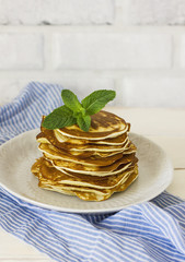 Stack of fresh baked pancakes with mint in white plate on blue linen on white background