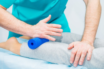 Woman at the physiotherapy receiving roller massage from therapist. A chiropractor treats patient's leg, caviar in medical office. Neurology, Osteopathy, chiropractic. Selective focus, Close up.