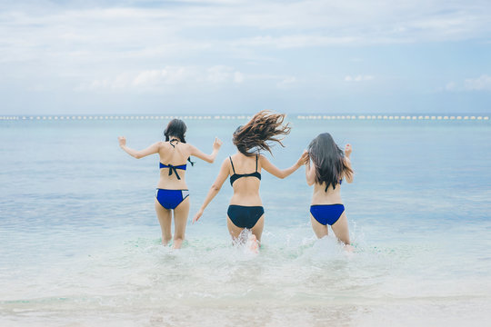 Three pretty beautiful asian women wearing colourful swimwear bikini with hat having fun and relax sunbathing on the beach in the summer