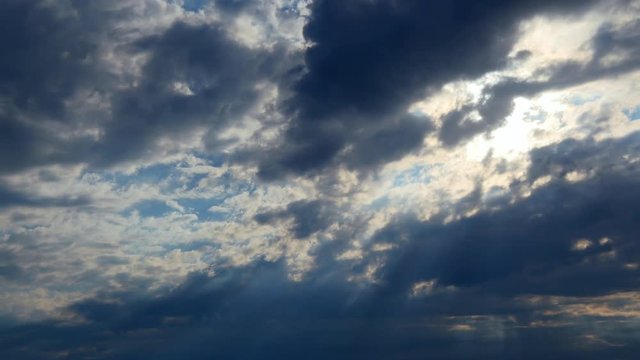 Sun rays shine through rain clouds. Beautiful timelapsed sunset through moving layers of clouds as a weather background. Sunset clouds. 4K, UHD, Timelapse. Beams of sunshine filter through clouds at s