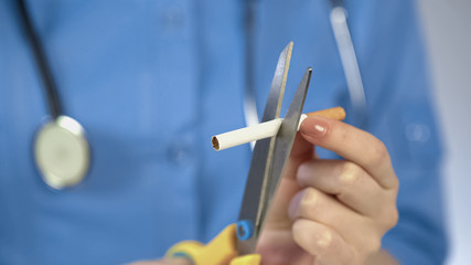 Doctors hands cutting cigarette with scissors, anti-tobacco campaign, bad habit