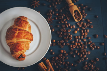black, strong coffee with croissants in a white dish sprinkled with cinnamon and anise on a blue table with a wooden texture