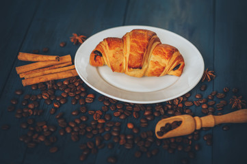 black, strong coffee with croissants in a white dish sprinkled with cinnamon and anise on a blue table with a wooden texture