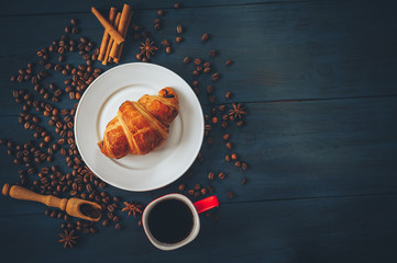 black, strong coffee in a red cup, with croissants in a white dish sprinkled with cinnamon and anise on a blue table with a wooden texture