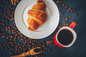 black, strong coffee in a red cup, with croissants in a white dish sprinkled with cinnamon and anise on a blue table with a wooden texture