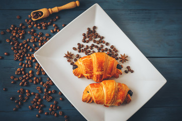 black, strong coffee with croissants in a white dish sprinkled with cinnamon and anise on a blue...