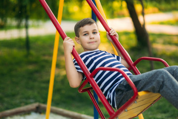 A little boy in a striped T-shirt is playing on the playground, Swing on a swing