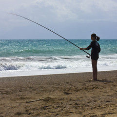 Young girl is fishing on the beach on the blue sea shore