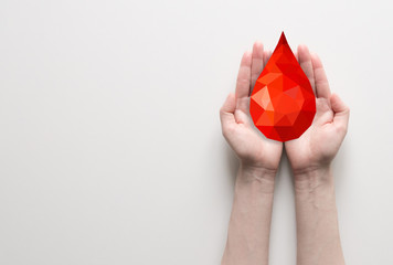 Two hands holding red polygonal blood drop, blood donation concept. Poster with place for text for clinic, hospital. - obrazy, fototapety, plakaty