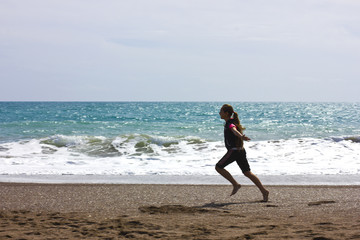 Fototapeta na wymiar Young girl runs and jumps on the beach near the blue sea