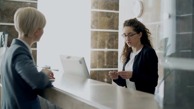 Blonde businesswoman talking with staff at reception in hotel and give key from room to receptionist girl. Business, travel and people concept