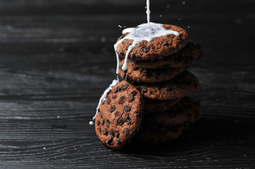 oatmeal cookies with chocolate and milk on a dark wooden background