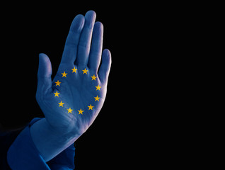 Hand with European flag showing stop gesture to prevent immigration of refugees, isolated on a black background with copy space