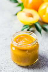 Yellow plum sauce in glass jar and fresh golden plums on concrete background. Selective focus, space for text. 