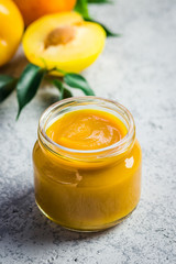 Yellow plum puree in glass jar and fresh golden plums on concrete background. Selective focus, space for text. 