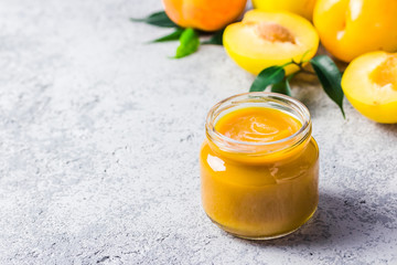 Yellow plum sauce in glass jar and fresh golden plums on concrete background. Selective focus, space for text. 