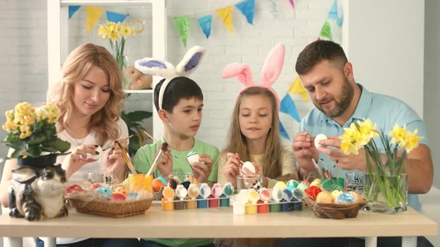 Mom, dad, son and daughter sitting and drawing on Easter eggs together
