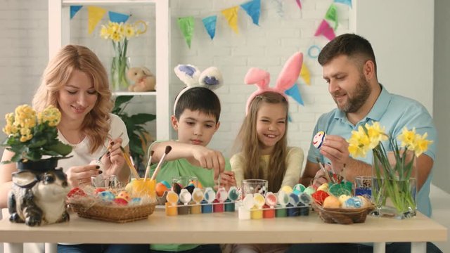 Funny family with kids wearing bunny ears painting eggs on Easter day