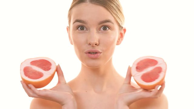 The woman holding two halves of a grapefruit on the white background