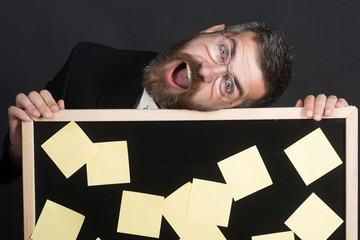 Obraz premium Business, management, planning, reminder, advertisement, people concept - cheerful businessman in glasses hold black board with stickers.Smiling man in suit laid head on board on which pasted stickers