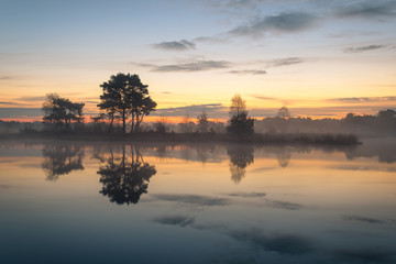 Fototapeta na wymiar Beautiful misty morning with nice colors in the sky and great refelctions on the lake. Taken at Putse Moer on The Kalmthoutse Heide in Belgium.