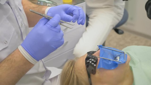 Dentist is treating a patient in a modern dental office. Orthodontist works with an assistant. The operation is carried out using a cofferdam. The client is inserted and restored teeth, make a denture