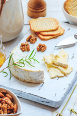 Cheese plate served with crackers, honey and nuts. Camembert on white wood serving board over white texture background. Appetizer theme.