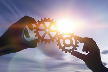 two hands of businessmen collect the gear from the gears of the details of the puzzles. against the background of sunlight. Concept business idea. Teamwork, cooperation, strategy