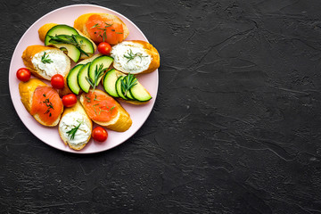 Healthy lunch with mini sandwiches cheese, fish and avocado on black background top view space for text