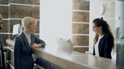 Receptionist girl talking with arrived businessman and businesswoman guests about check-in in hotel and giving key card from room to man . Business, travel and people concept