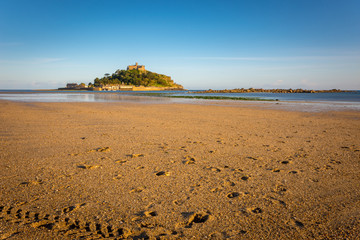 Sand, water and rocks of Marazion Beach with castle on hill