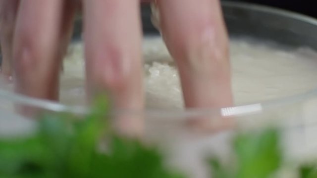 Close up shot of male hand mixing rice with water in transparent glass bowl, tracking left