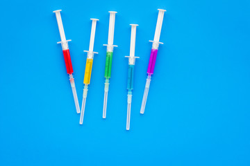 Vaccination, immunization. Syringe with colored medicament on blue background top view copy space